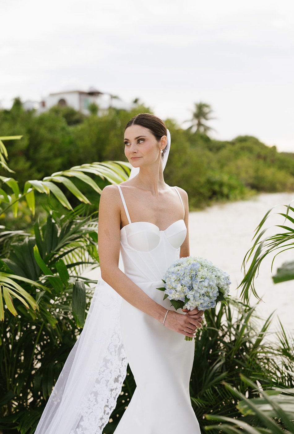 Bride in corset gown with blue hydrangea bouquet — destination beach wedding glam